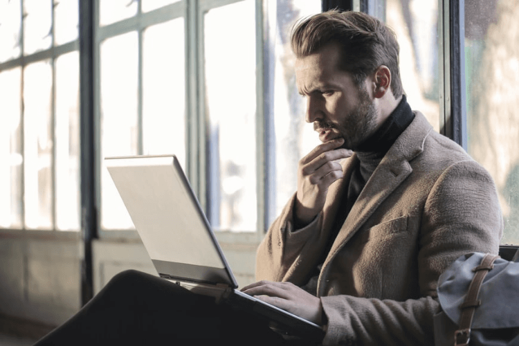 Homem utilizando laptop enquanto reflete sobre possíveis estratégias para a empresa.